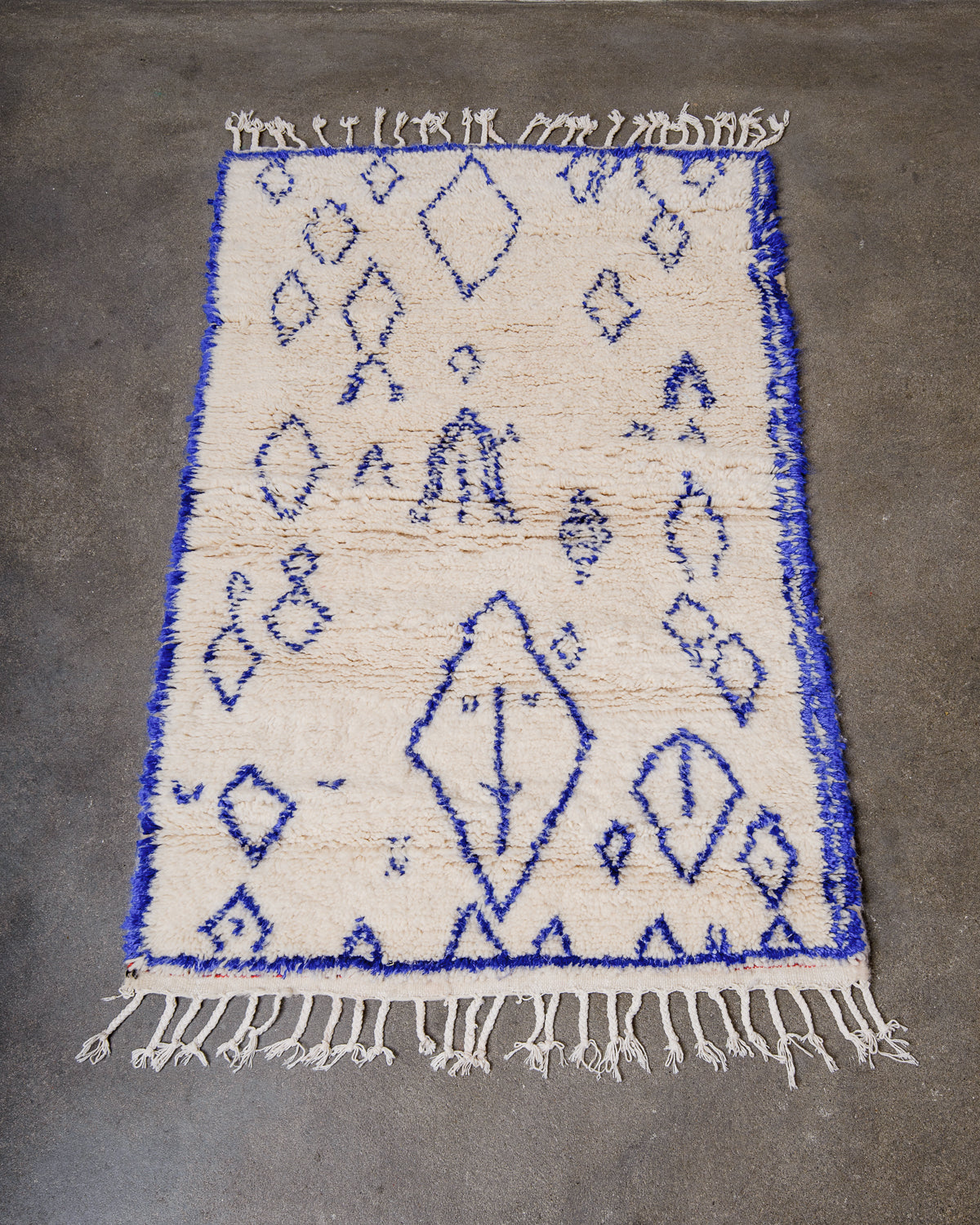 Cream wool Azilal rug with blue cotton design laying on a concrete floor.